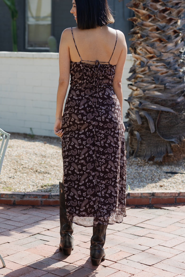 Woman wearing a floral dress standing on a brick patio.