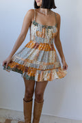 Woman wearing a patterned dress with orange and green tones against a white background