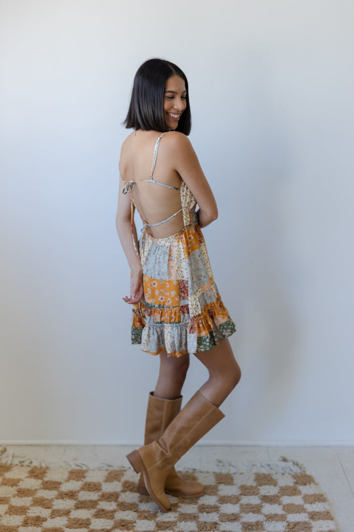 Woman wearing a patterned dress and brown boots standing on a checkered rug.