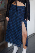 Person wearing a blue plaid skirt with a high slit, standing indoors.