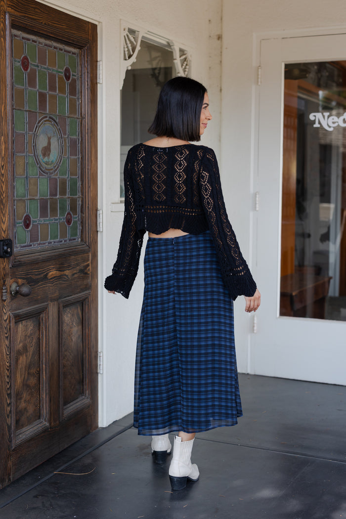 Woman in a blue plaid dress standing in front of a door with a stained glass panel.