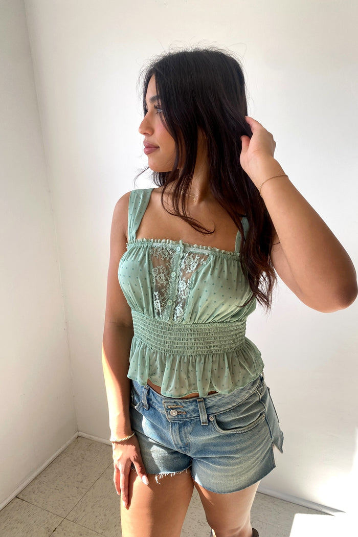 Woman wearing a green lace top and denim shorts against a plain background