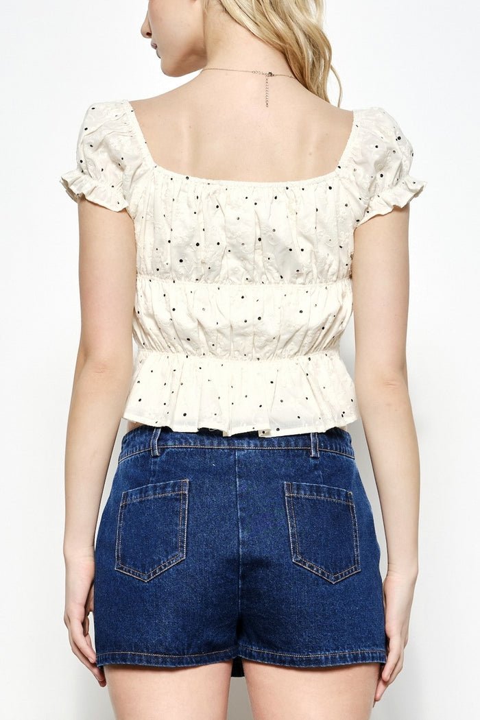 Person wearing a white blouse with ruffled sleeves and blue denim shorts on a plain background