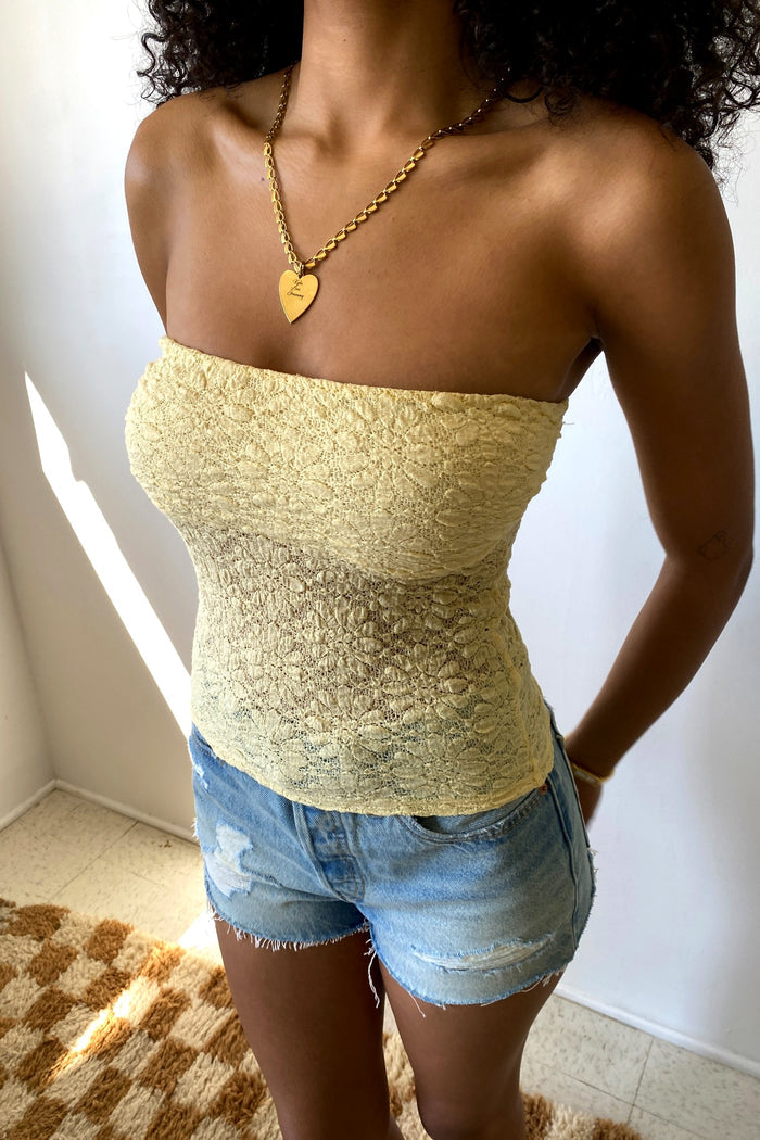 Person wearing a strapless top and denim shorts with a gold necklace.