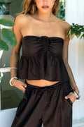 Woman wearing a brown strapless top and high-waisted pants with plants in the background