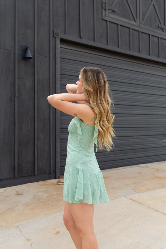 Woman in a light green dress standing in front of a dark wooden door.