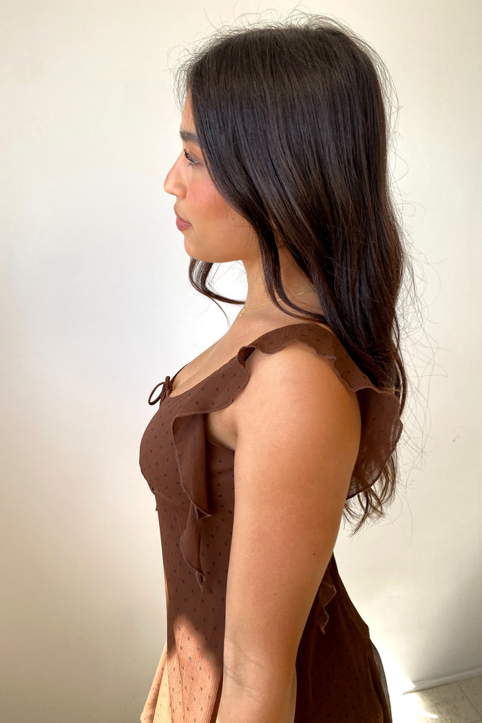 Woman wearing a brown dress with ruffled shoulders against a plain background