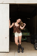 Woman in a brown top and white shorts standing in an open garage.