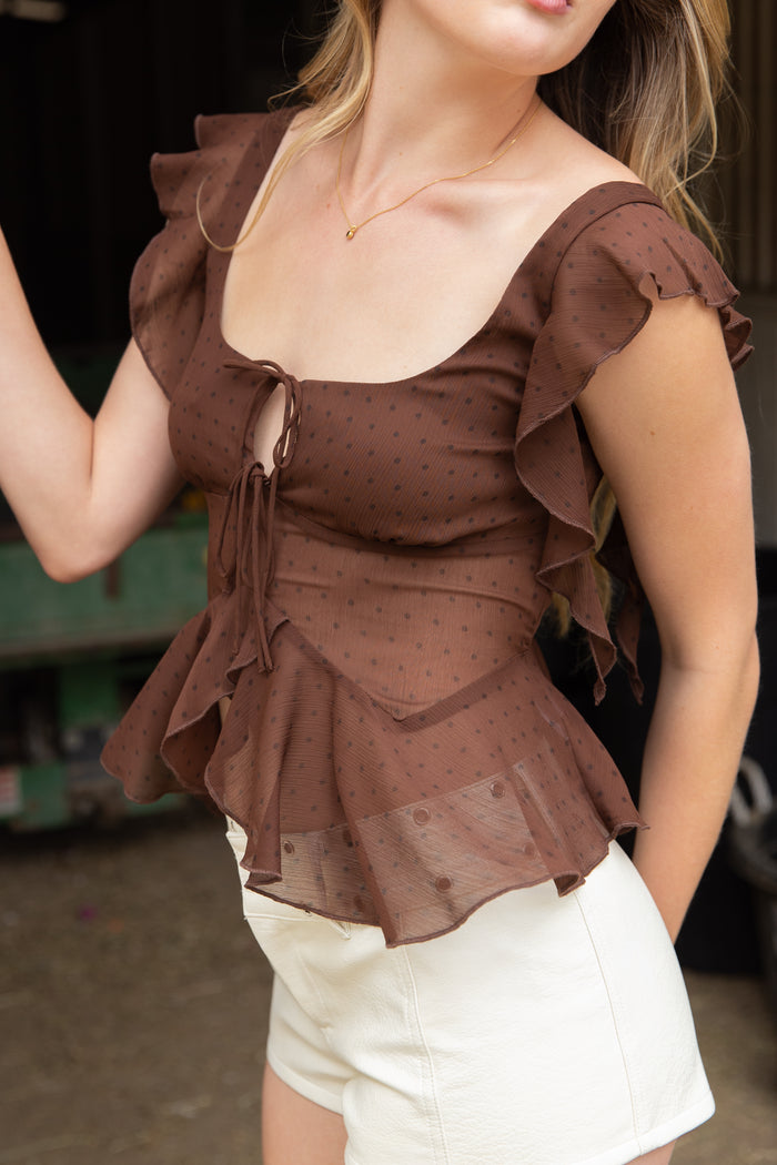 Woman wearing a brown ruffled top with a blurred background