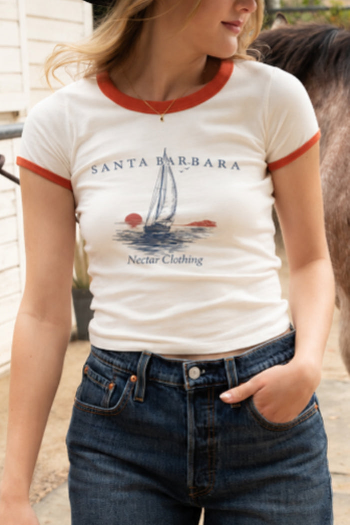 A woman wearing a Santa Barbara ringer t-shirt with a sailboat graphic and 'Nectar Clothing' text, paired with dark blue jeans.