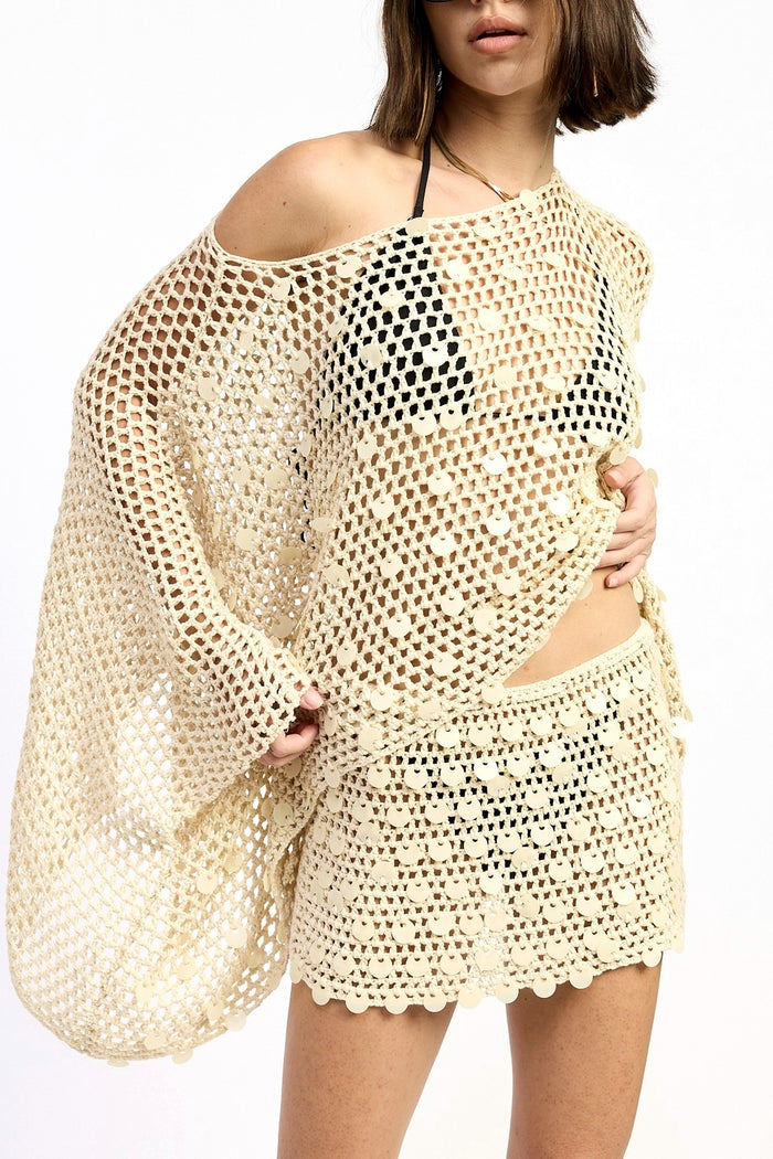 Woman wearing a beige crochet cover-up over a black bikini on a white background