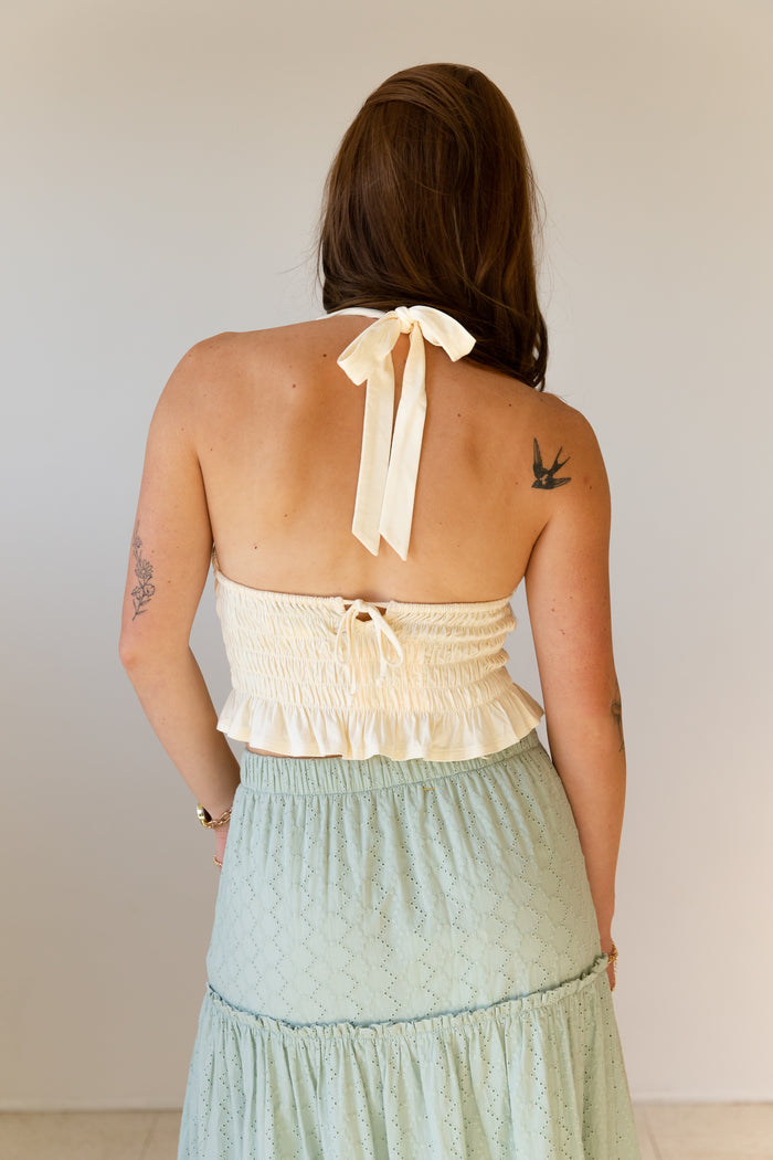 Woman wearing a light-colored halter top and green skirt against a plain background