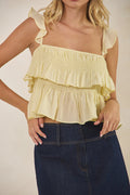 Woman wearing a yellow ruffled top and dark blue jeans on a beige background