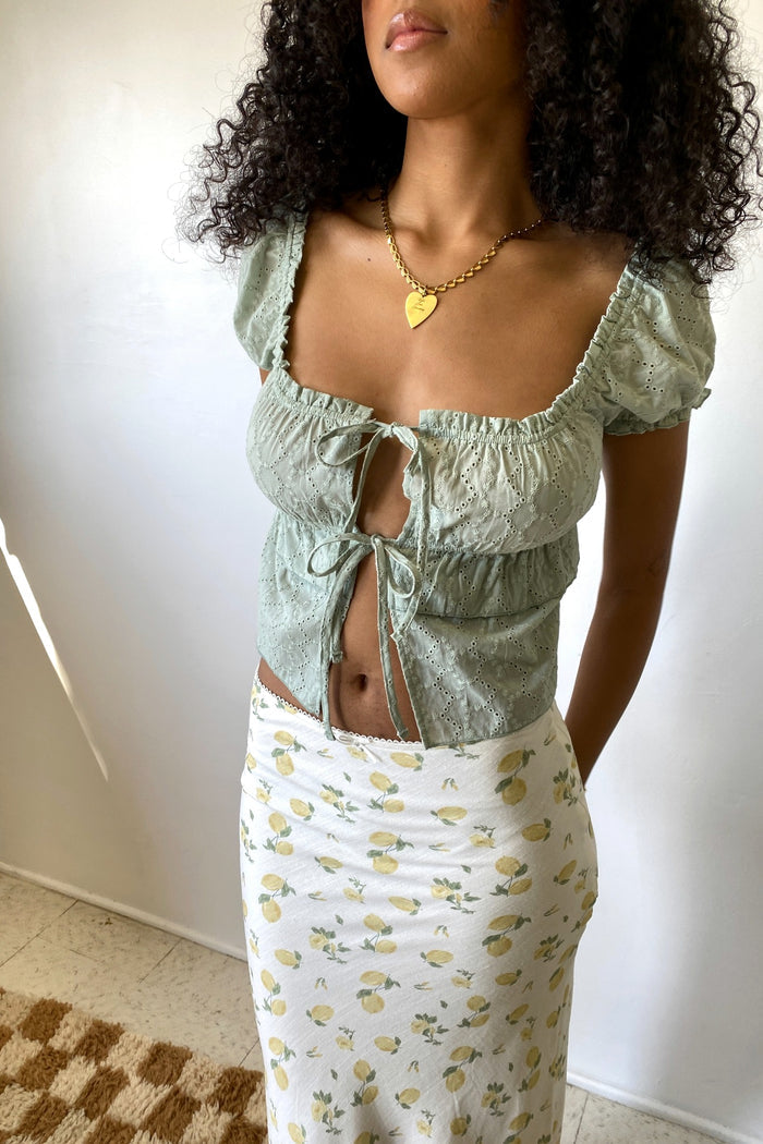 Woman wearing a green top with ruffled sleeves and a floral skirt against a plain background