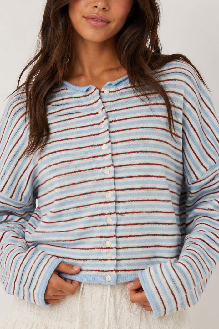 A woman wearing a fuzzy knit cardigan with horizontal light blue, white, and rust-red stripes, featuring a button-up front and a relaxed fit.