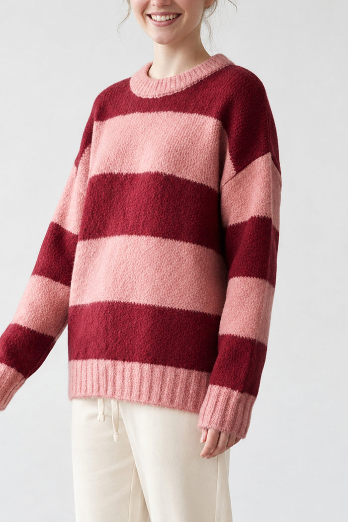 A woman wearing a fuzzy knit sweater with horizontal stripes in deep burgundy and light pink, paired with cream-colored pants, against a plain light gray background.
