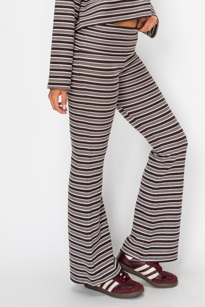 A person wearing loose, wide-leg striped pants and a matching long-sleeve top, paired with burgundy sneakers with white stripes, against a plain light gray studio background.