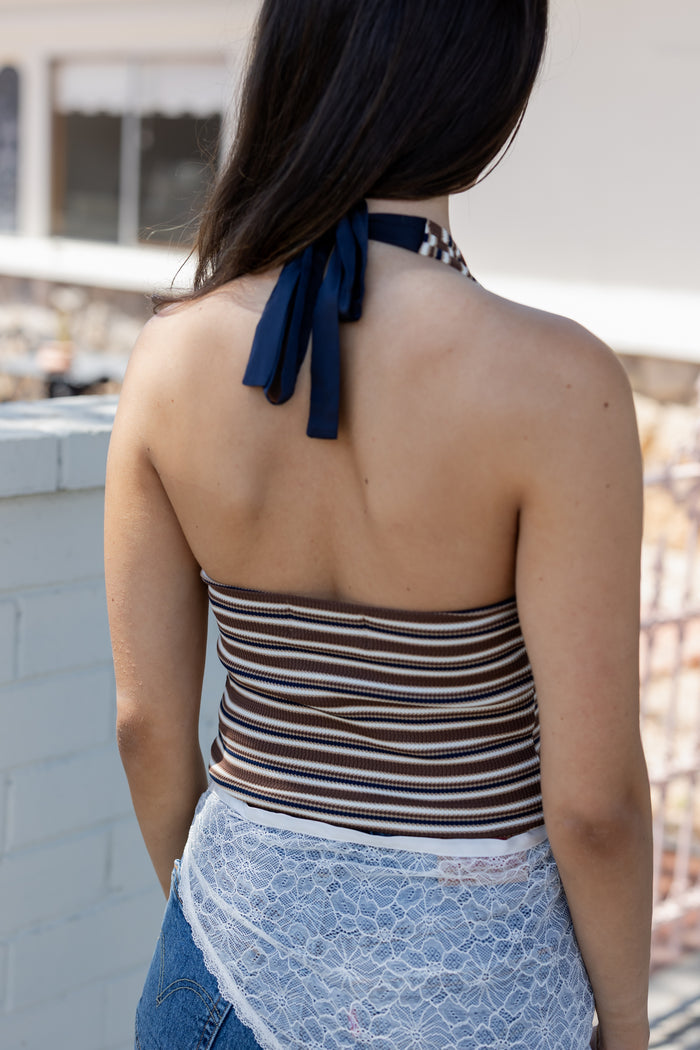 Woman wearing a striped halter top and blue jeans with a blurred background