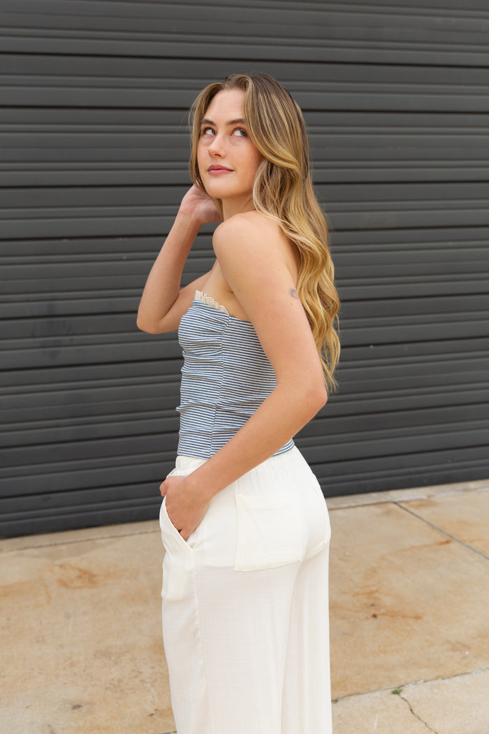 Woman wearing a striped top and white pants against a dark gray wall.