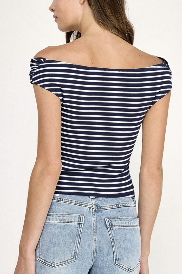Woman wearing a navy and white striped top with off-shoulder design and light blue jeans.