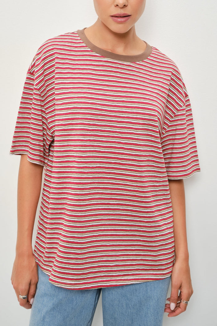 A person wearing an oversized short-sleeve striped t-shirt with horizontal red, white, and thin brown stripes, featuring a solid brown crew neck, paired with light blue jeans.