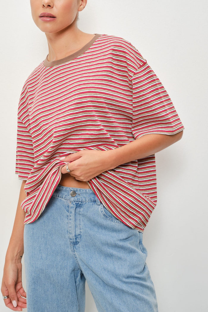 A person wearing an oversized short-sleeve striped top with red, pink, and white horizontal stripes and light blue jeans, photographed against a plain light background.