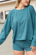 A woman wearing a matching teal long-sleeve ribbed top and shorts set, photographed outdoors against a light brick wall.