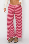 A person wearing loose, wide-leg knit pants with horizontal pink and red stripes, paired with a white cropped top and tan slip-on shoes, against a plain white studio background.