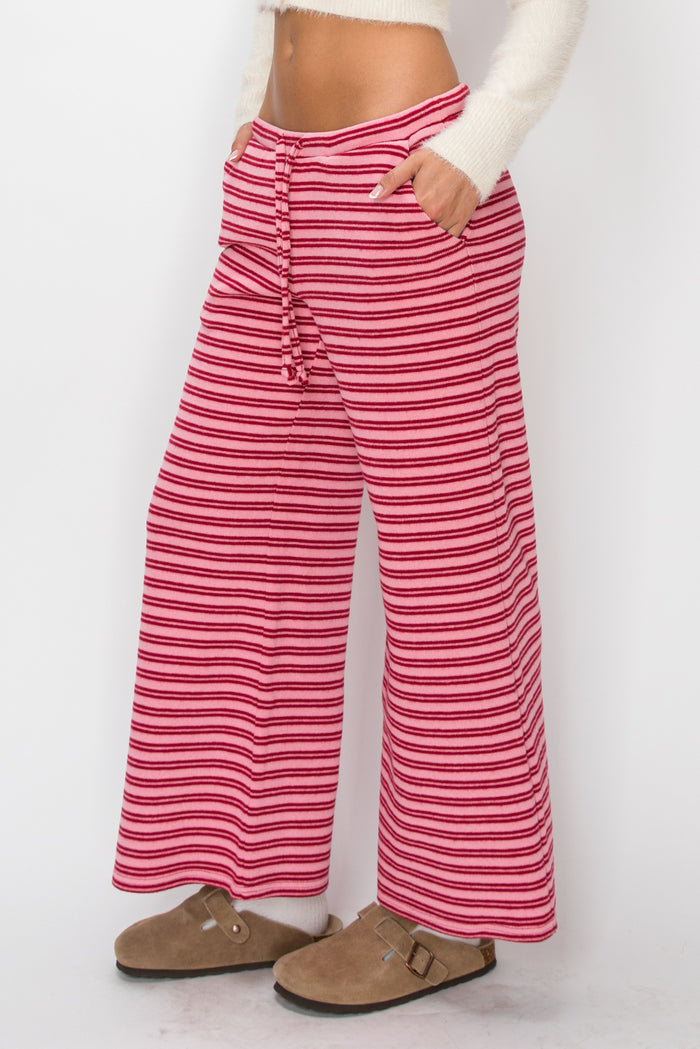 A person wearing red and white horizontally striped wide-leg pants with a button fly, paired with a white long-sleeve top and brown clogs, shown from the waist down against a plain white background.