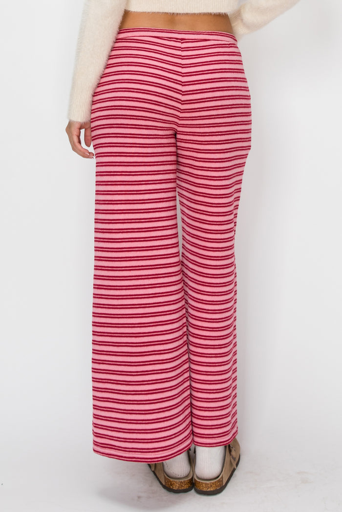 A person shown from the back wearing wide-leg knit pants with horizontal pink and white stripes, paired with a cream sweater and brown shoes, against a plain white background.