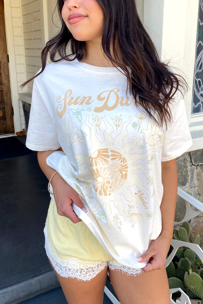 Person wearing a white t-shirt with gold text and design, standing outdoors.