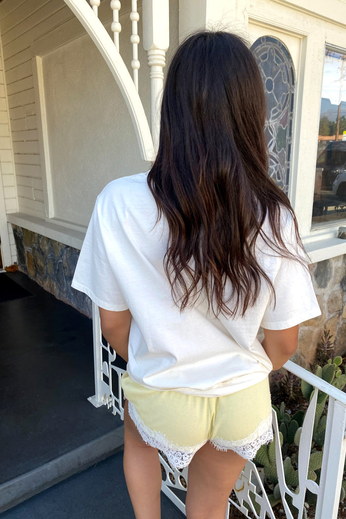 Person wearing a white t-shirt and yellow shorts with lace trim on a porch.