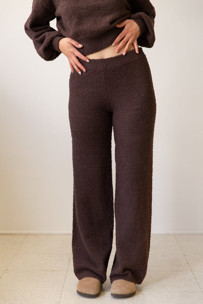 Person wearing brown knitted pants and sweater against a white background