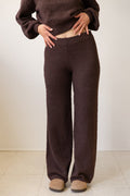 Person wearing brown knitted pants and sweater against a white background