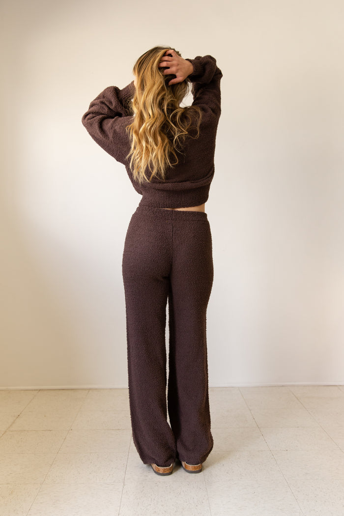 Person wearing a brown outfit standing against a white wall.