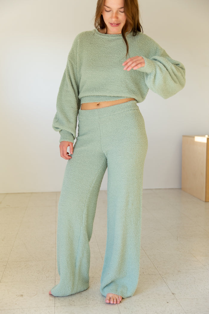Woman wearing a green outfit standing in a minimalistic room.