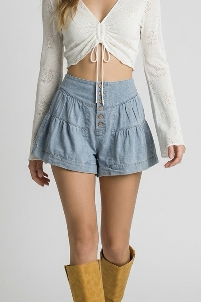Person wearing a white top, denim shorts, and yellow boots on a plain background