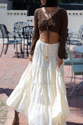 Woman wearing a brown cardigan over a white tiered skirt in an outdoor setting.