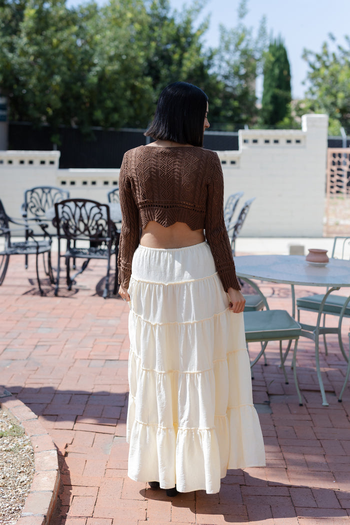 Woman wearing a brown cropped top and white tiered skirt standing on a patio.