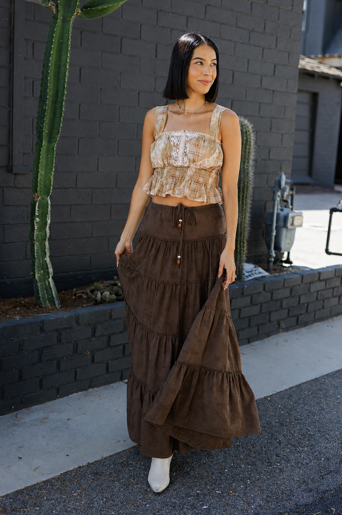 Woman in a brown tiered skirt and beige top standing in front of a brick wall with cacti.