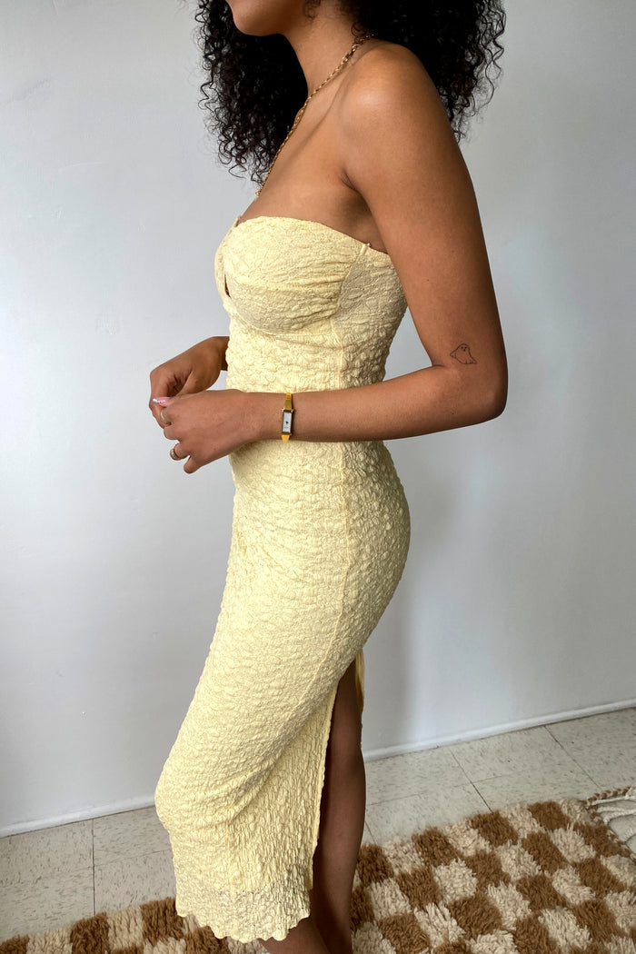 Woman wearing a yellow strapless dress with a slit, standing against a plain background.