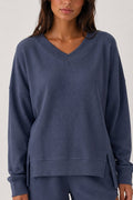 A woman wearing a textured waffle-knit long-sleeve sweater in a muted slate blue color, shown from the chest down against a plain light background.