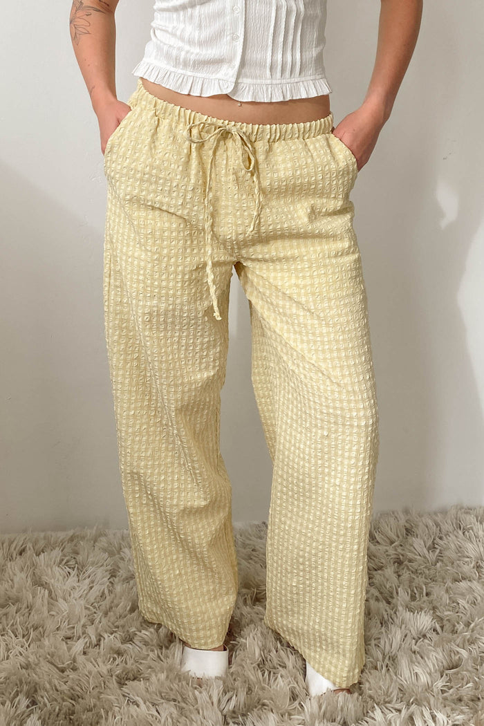 Person wearing yellow checkered pants on a textured surface with a neutral background