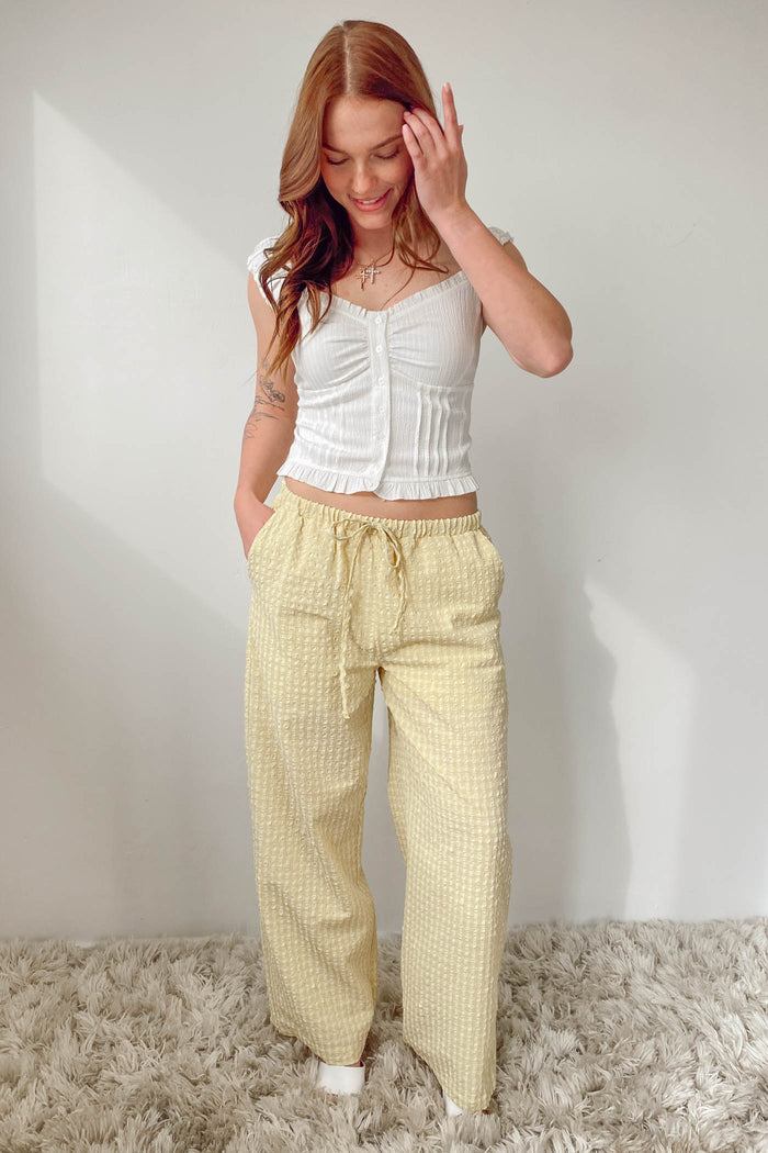 Woman wearing a white top and yellow checkered pants against a plain background